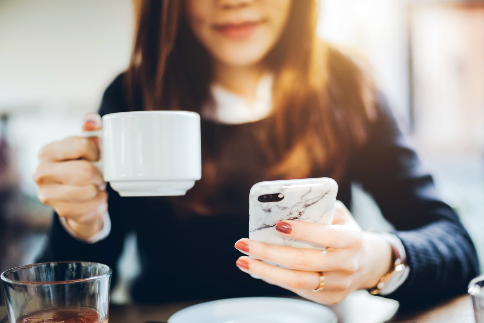 Close up of young woman having coffee and reading news on mobile phone in the early morning before work