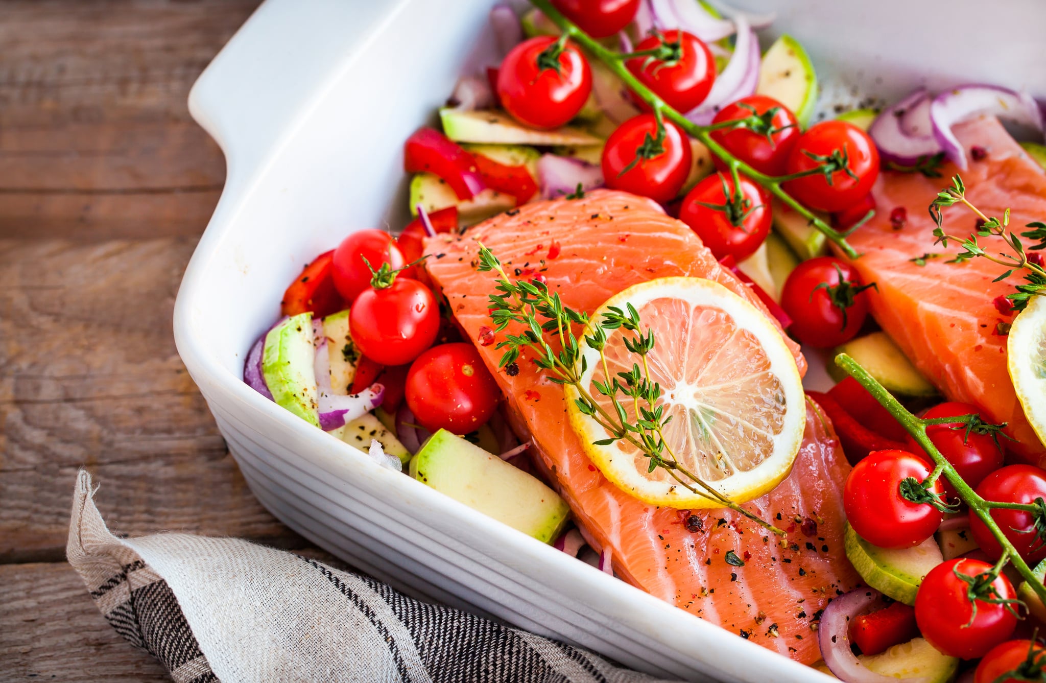 Raw fresh delicious salmon, cherry tomatoes, onion, courgette, pepper and lemon in pan, ready to cook