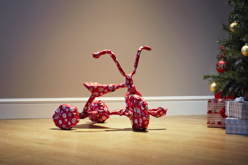 Child's bicycle wrapped in Christmas paper on floor next to christmas tree and presents
