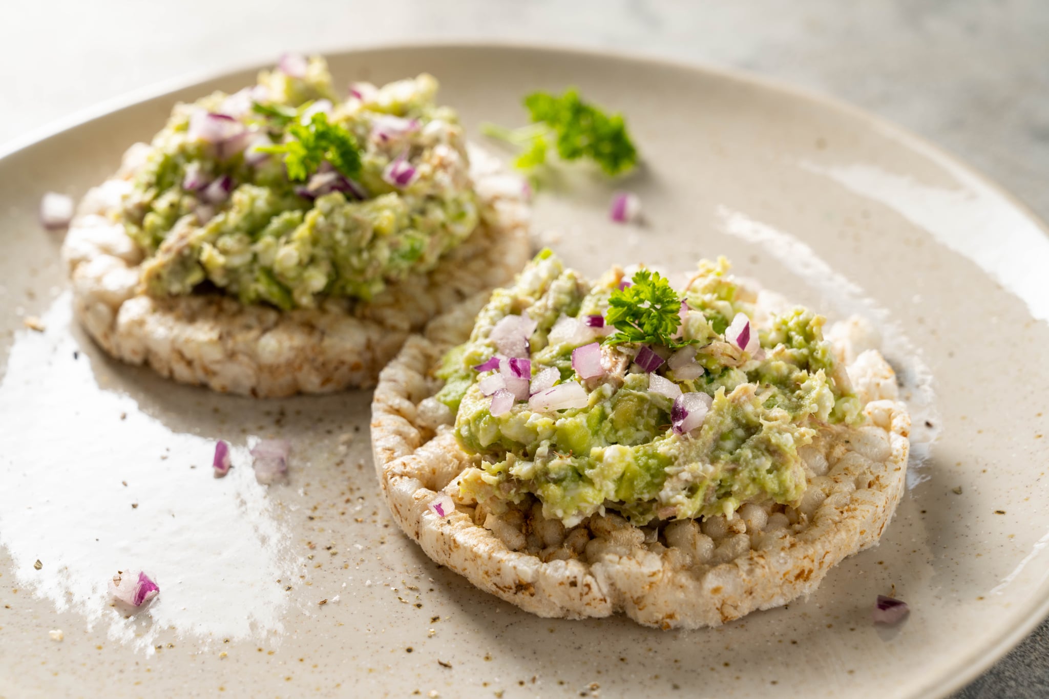 Rice cake with avocado and tuna salad with red onion.