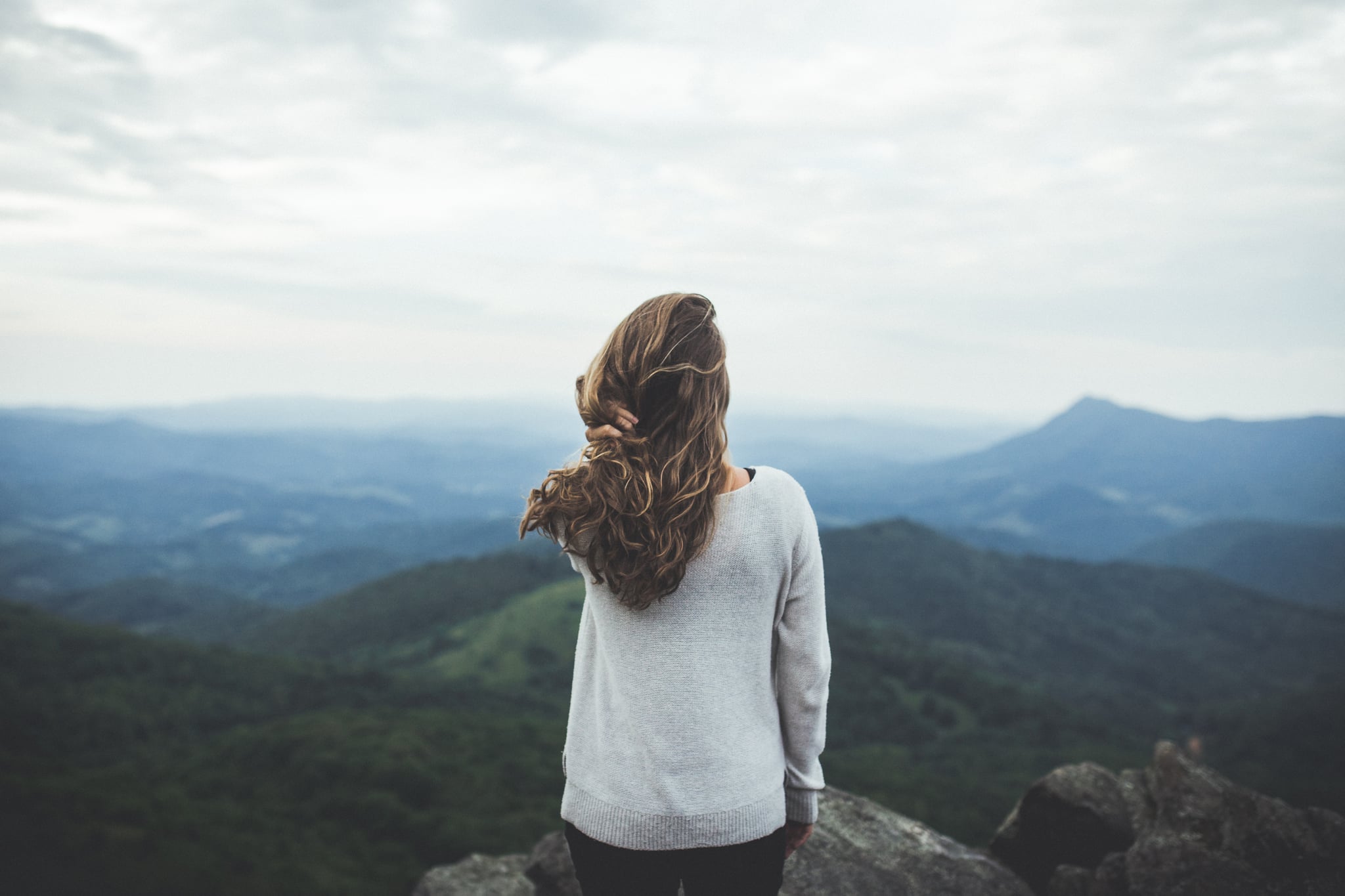 A woman reaches the summit of a mountain with a large sky overhead.