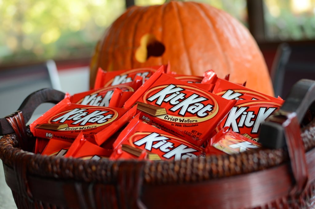 A basket overflowing with Kit-Kat bars sit in front of a partially visibly Jack-o-lantern