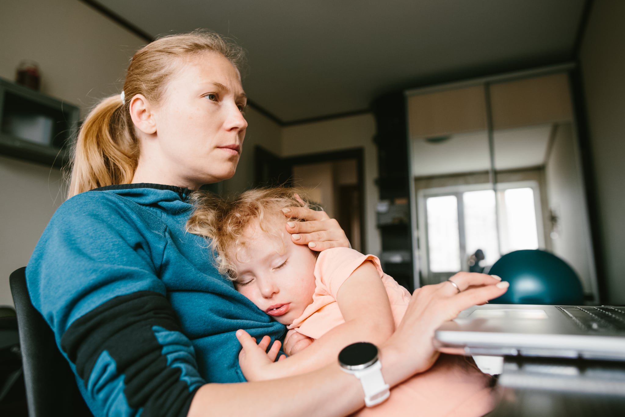 COVID-19 working from home.A woman with a sleeping child in her arms sits at a computer and works remotely.