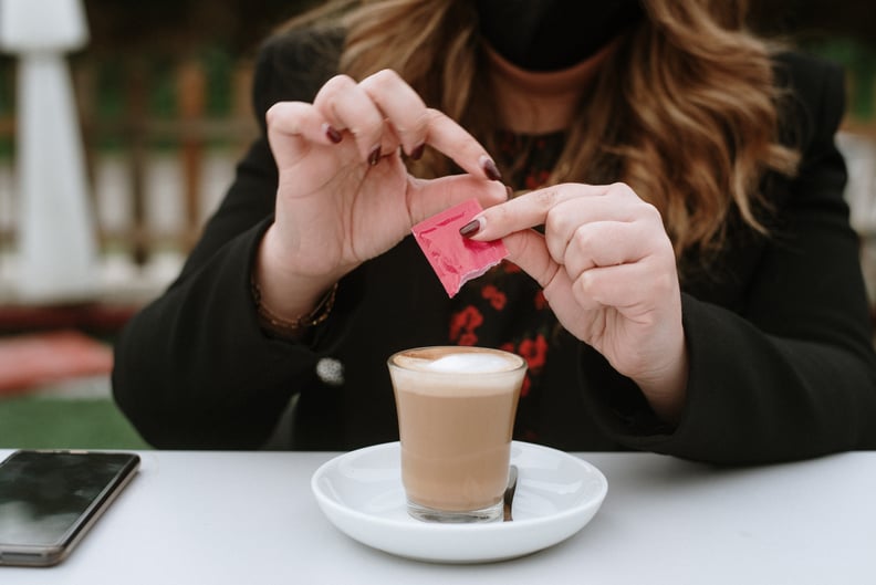 A young woman having a coffee and pouring in artificial sweetener packet.