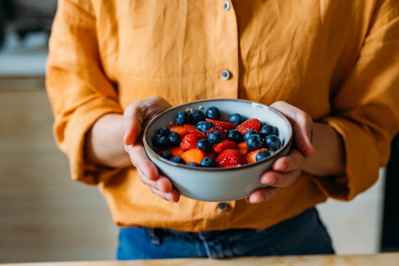 Close-up of a person holding a bowl filled with fresh strawberries and blueberries.