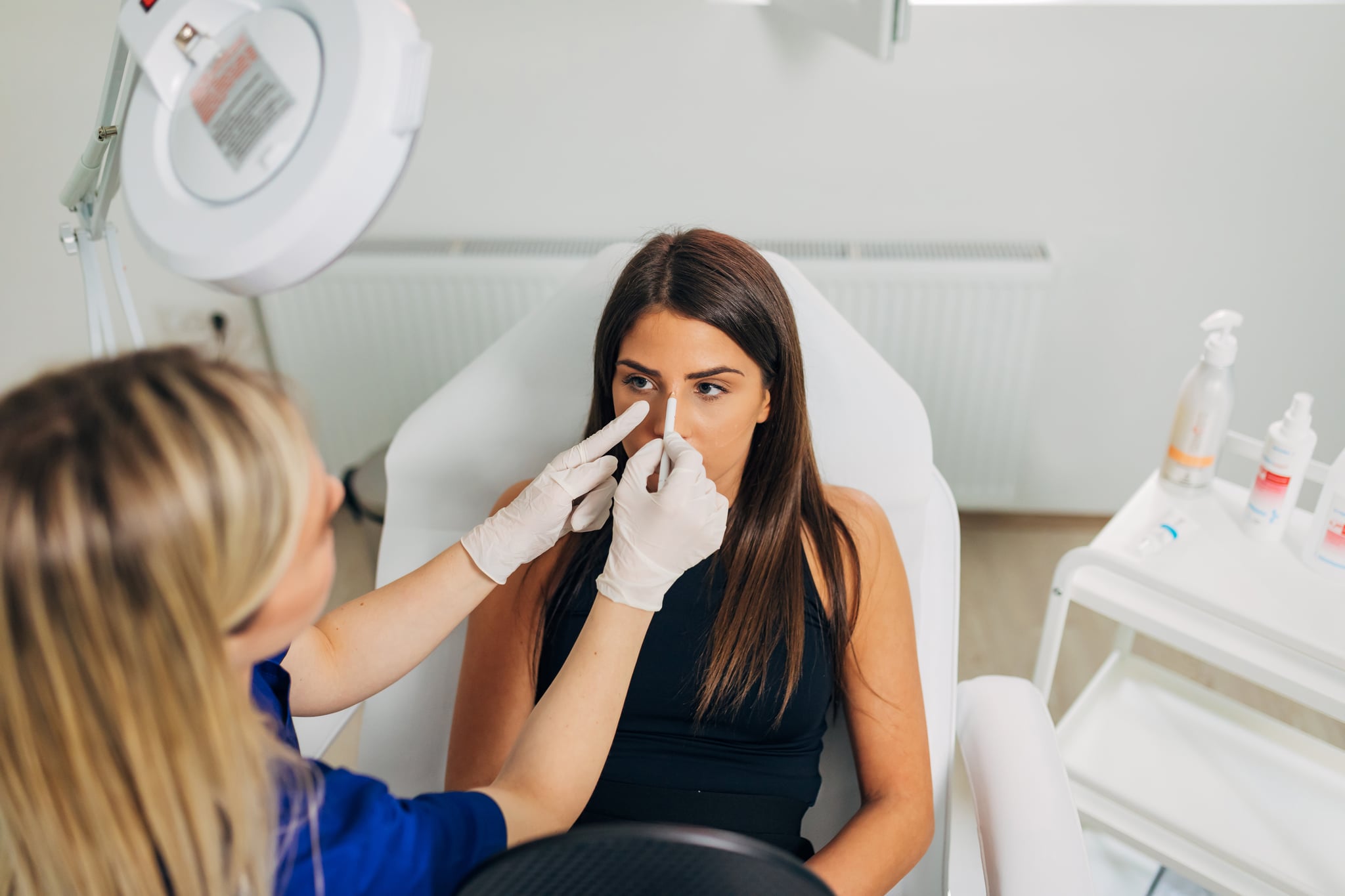 In the modern dermatology clinic, dermatologist and beautician, using the white pen, to mark and select areas she gonna fill with the dermal materials in her young female patient to lift that part