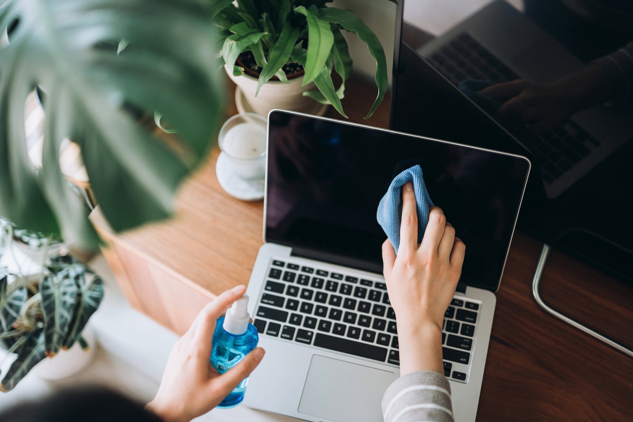 Cropped shot of a young woman cleaning the surface of laptop with cleaning spray and antistatic cloth at home