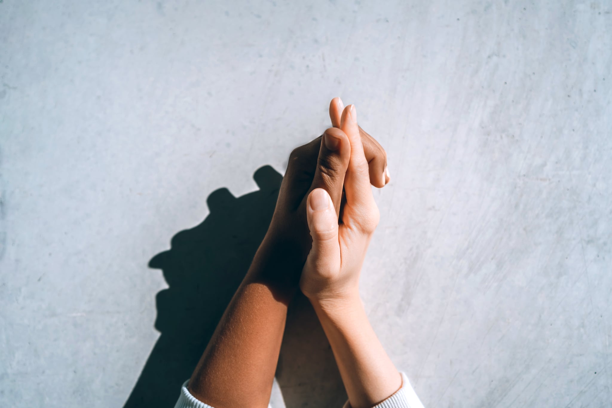 Two people holding hands against a concrete gray wall