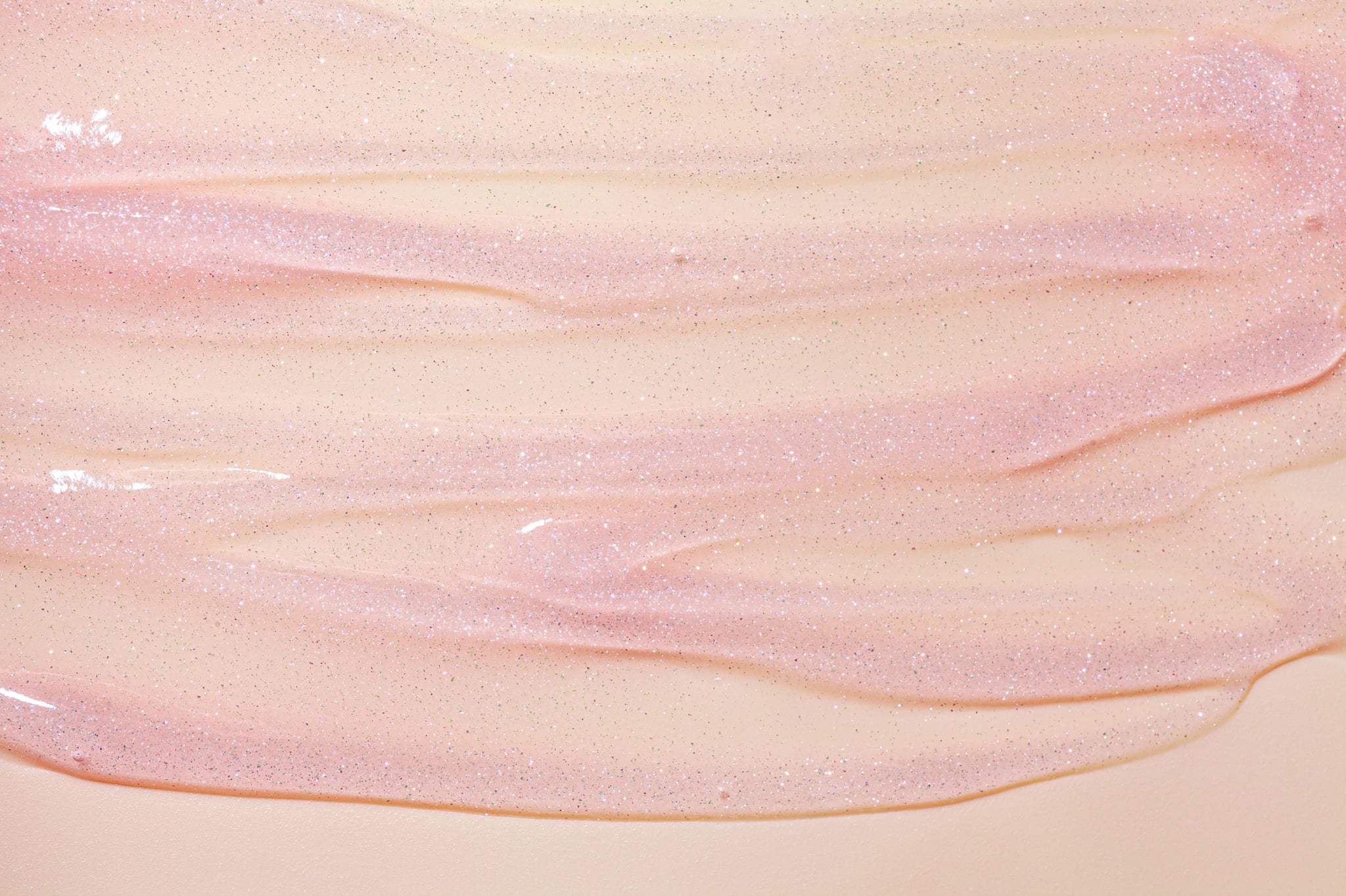 Pink shimmery lip gloss glitter texture on vanilla beige background.