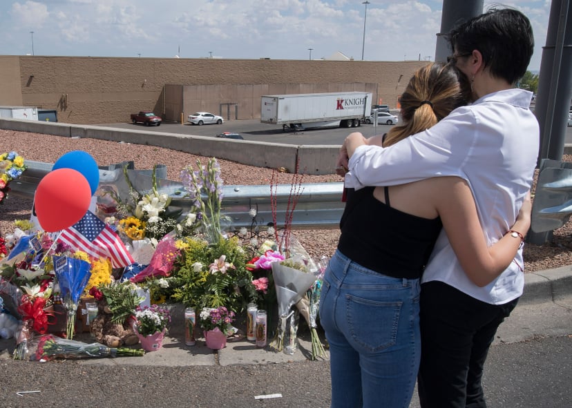 People hug beside a makeshift memorial outside the Cielo Vista Mall Wal-Mart (background) where a shooting left 20 people dead in El Paso, Texas, on August 4, 2019. - Texas authorities are investigating the Saturday mass shooting at a Walmart store in El 