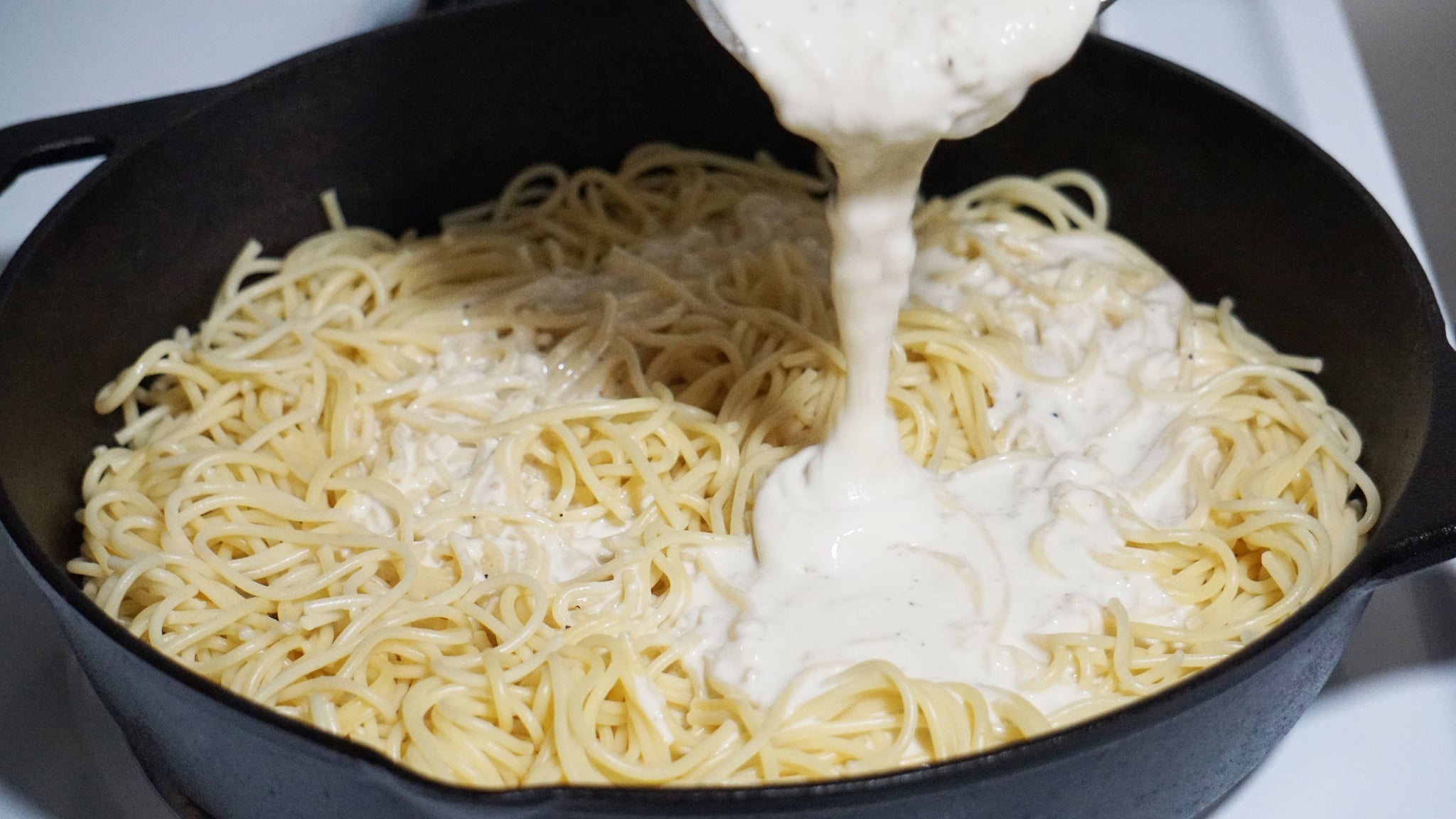 million dollar spaghetti recipe: pouring alfredo over pasta