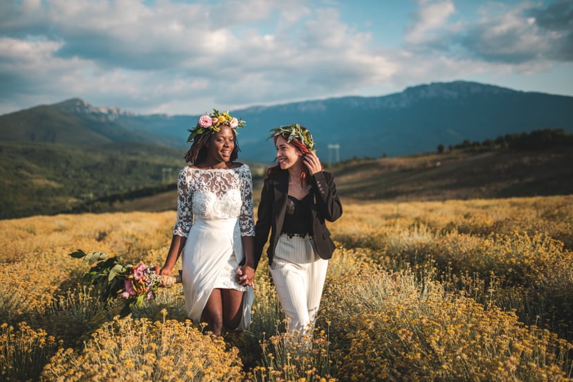 Two beautiful, young women holding hands and walking on meadow on their wedding day