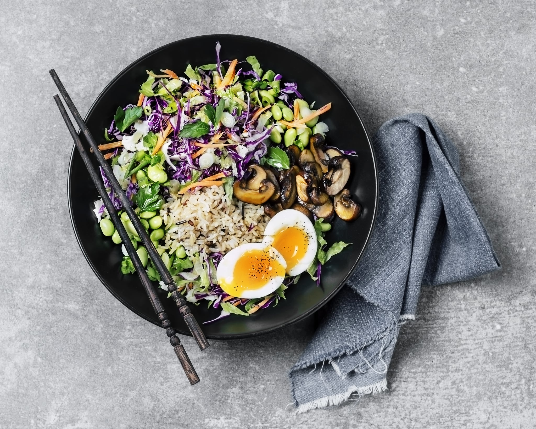 A bowl of fresh salad with fried rice, and boiled eggs on grey background