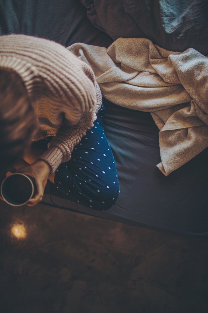 Photo of a young woman drinking her first cup of coffee still sitting in her bed, in pajamas