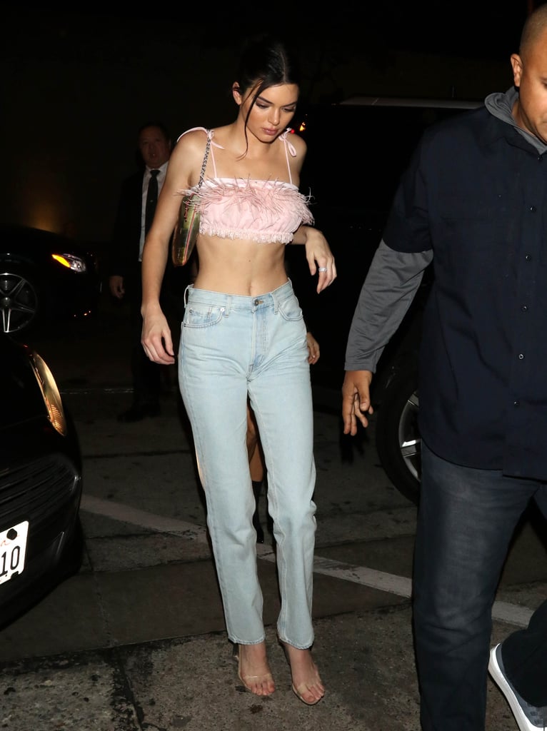 In February, Kendall wore a fabulous feathered bra to to dinner. She paired it with sleek Yeezy basics including high-rise denim and PVC heels, a Louis Vuitton bag, and a stunning XIV Karats ring.