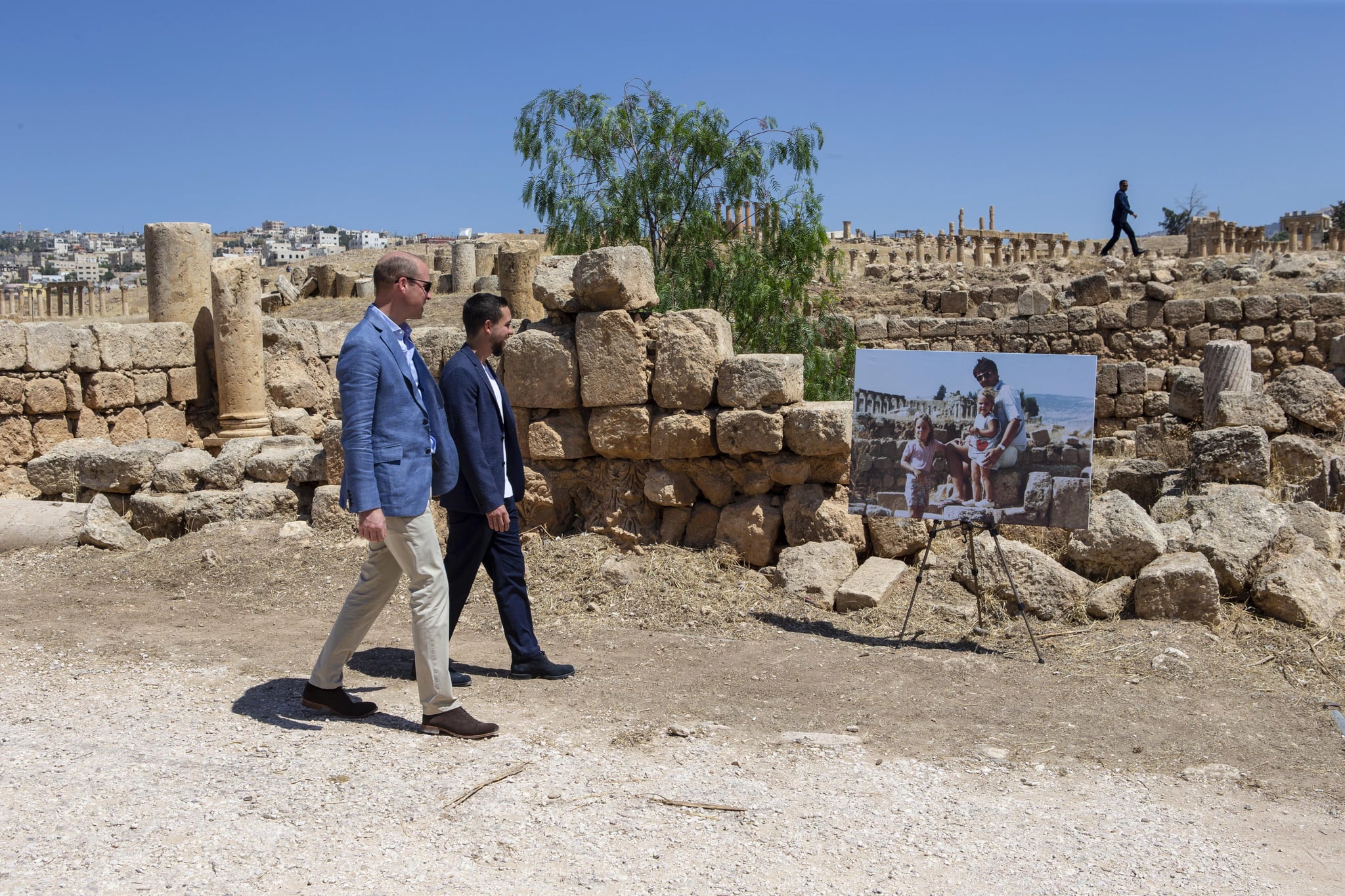 AMMAN, JORDAN - JUNE 25: Prince William, Duke of Cambridge and Crown Prince Hussein of Jordan walk past an enlarged photo of Catherine, Duchess of Cambridge in her youth with her father on a family holiday, as they visit the Jerash archaeological site on June 25, 2018 in Amman, Jordan. (Photo by Ian Vogler - Pool/Getty Images)