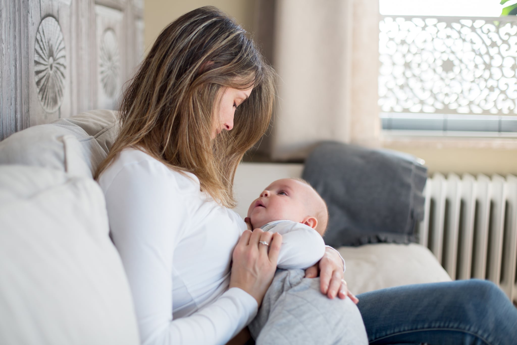 Young mother, holding her toddler boy, breastfeeding him at home, sunny living room