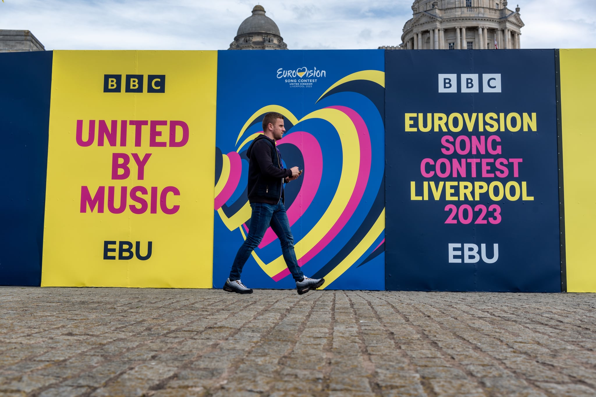 LIVERPOOL, MERSEYSIDE, UNITED KINGDOM - 2023/05/11: A man walks past a hoarding at the Eurovision village at Pier Head in Liverpool. The Eurovision Song Contest was won last year by Ukraine who are unable to host this year's contest due to the ongoing war with Russia. (Photo by Dave Rushen/SOPA Images/LightRocket via Getty Images)