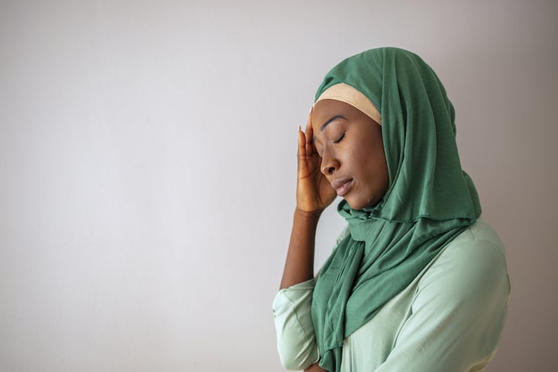 Muslim woman wearing hijab with hand on head dealing with fasting headaches