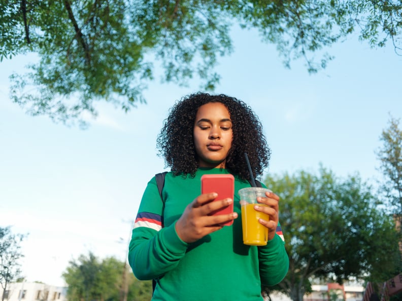 A college girl holding a healthy drink and texting outdoors.