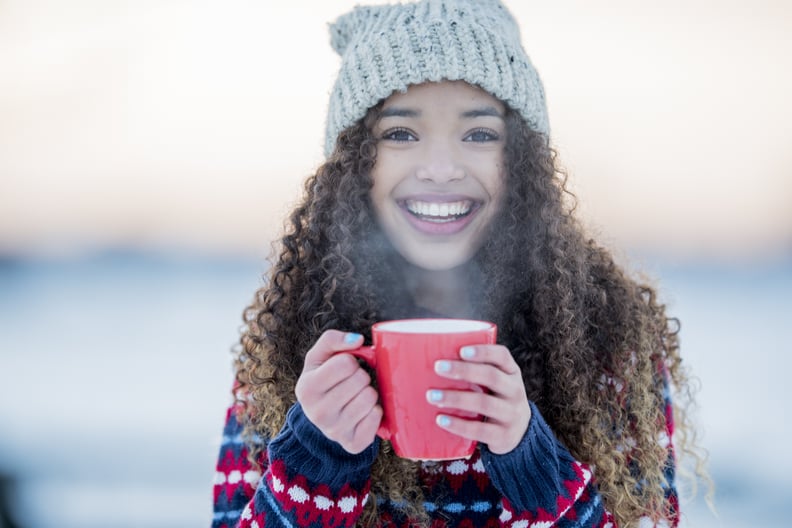 A young mixed race girl enjoys a cold winter day outside. She is smiling and holding a hot mug.