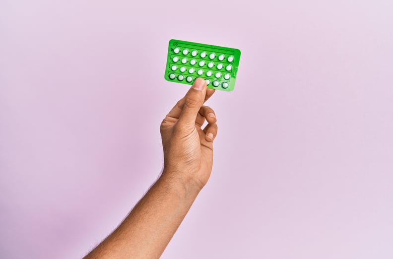 Young brown hand holding birth control pills over isolated pink background.