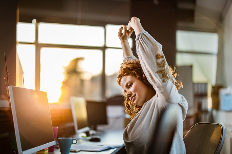 Young female programmer stretching her arms while working in the office.