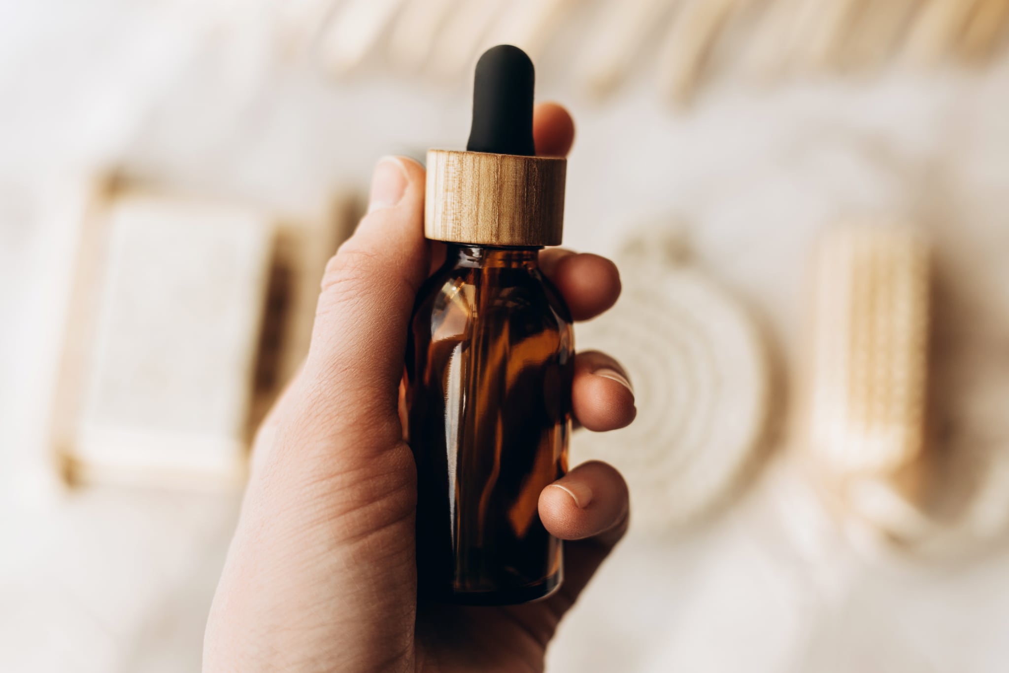 Brown cosmetic jar with a pipette in woman hand on a beige background.