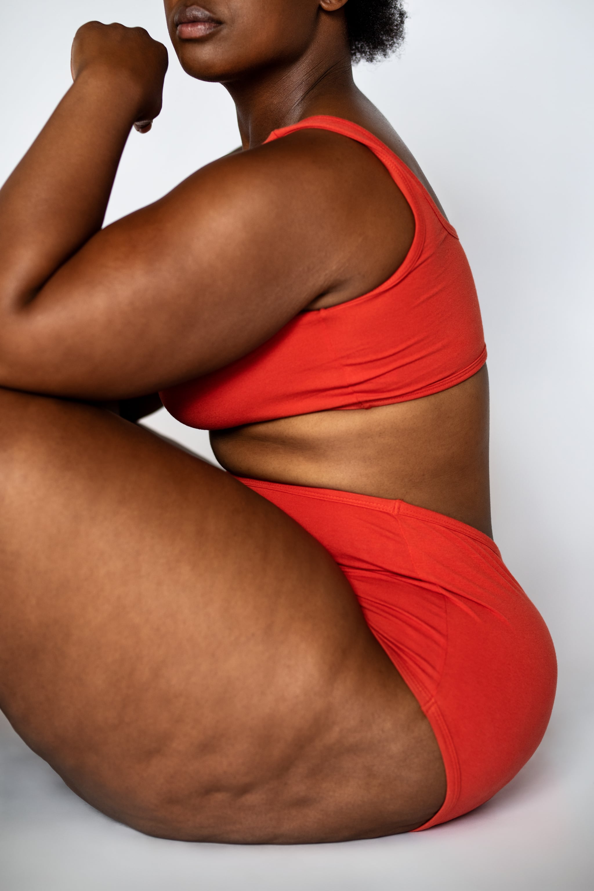 Plus size woman with fat legs sitting on floor. Oversized woman wearing lingerie with cellulite on thighs. Cropped shot.