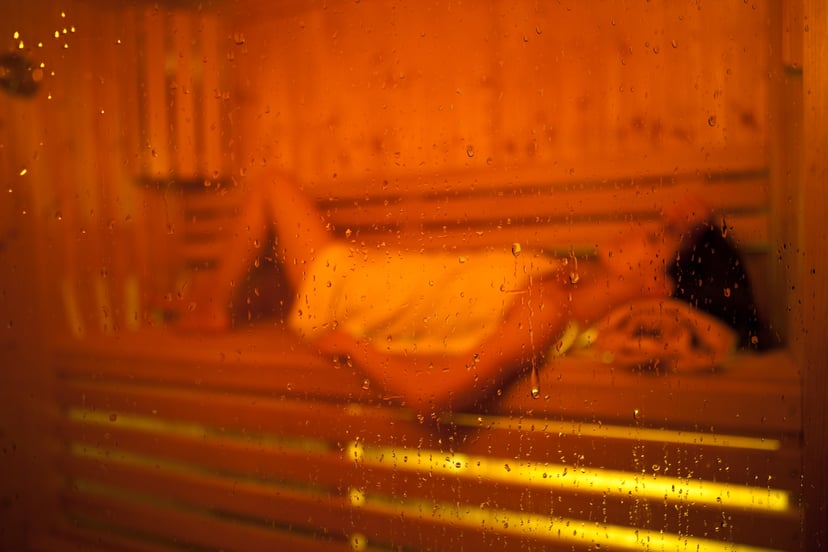 Girl in Sauna shot through glass sauna door. Focus is on the water droplets on the door.
