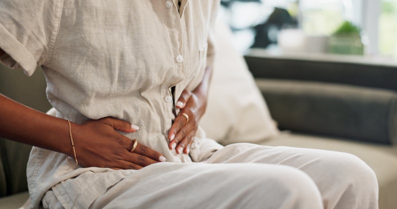 Woman dealing with bloating, sitting on the couch with her hands on her stomach.