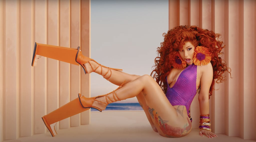 For perhaps her wildest look of the video, Cardi B wears a purple plunging one-piece covered in rhinestones, towering Carolin Holzhuber heels, and giant floral earrings.