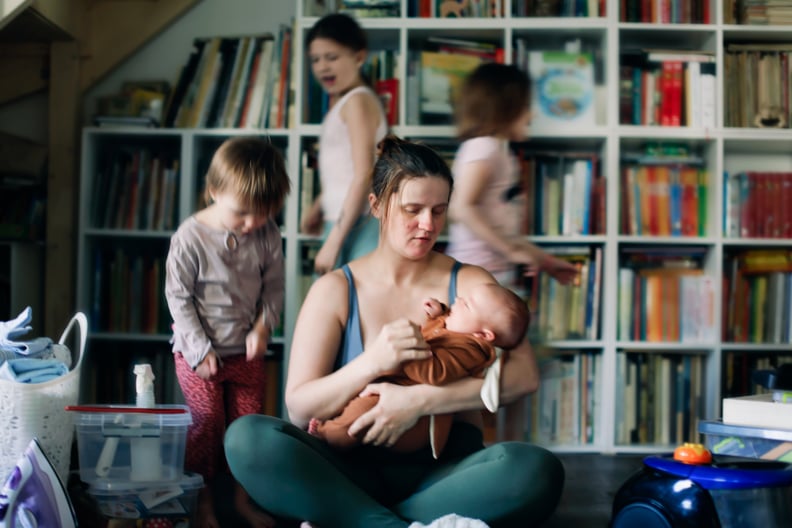 Busy mom holding a baby while three other children play nearby