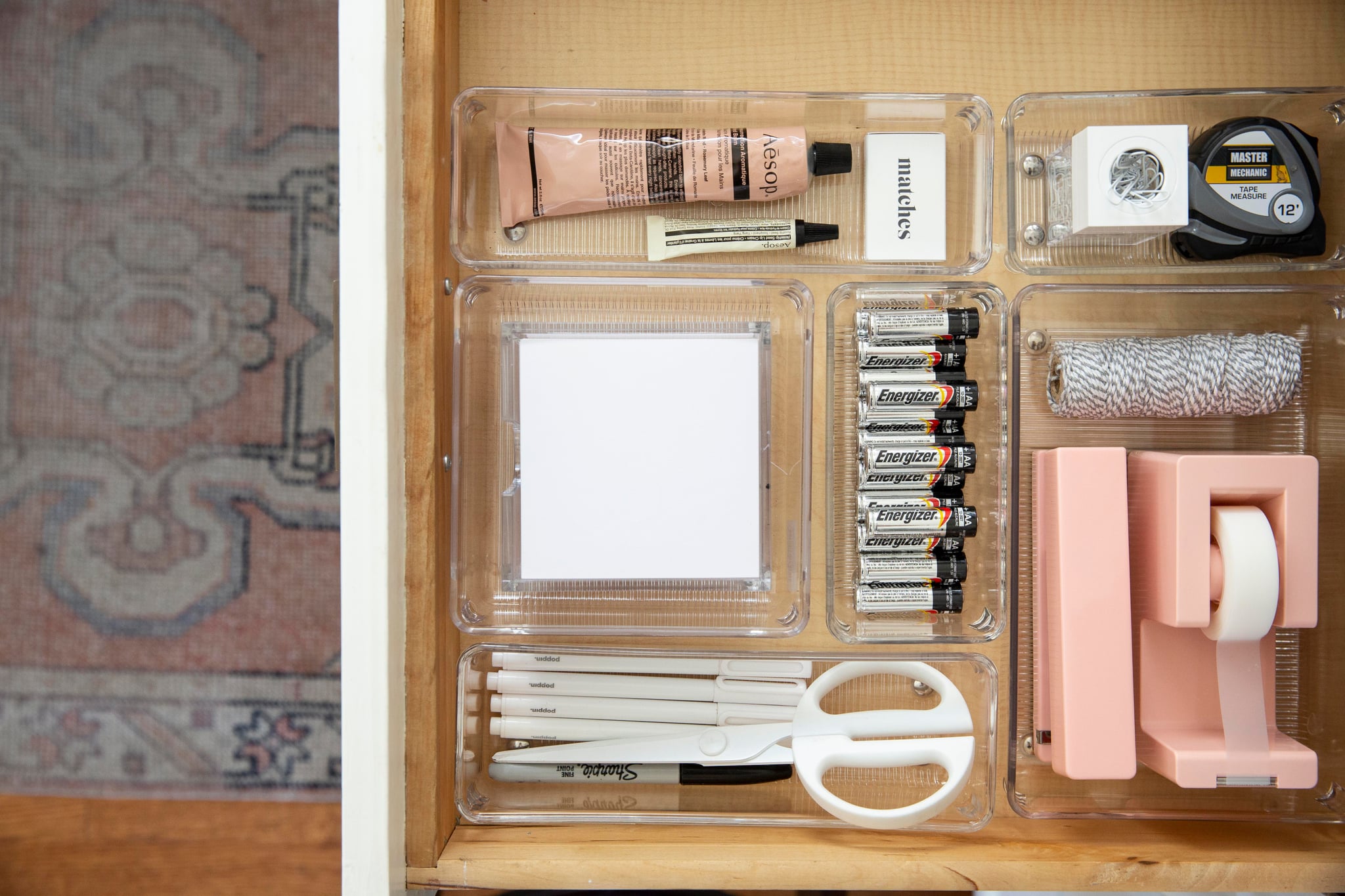 an organized desk drawer with tape, batteries, a stapler, and notepad