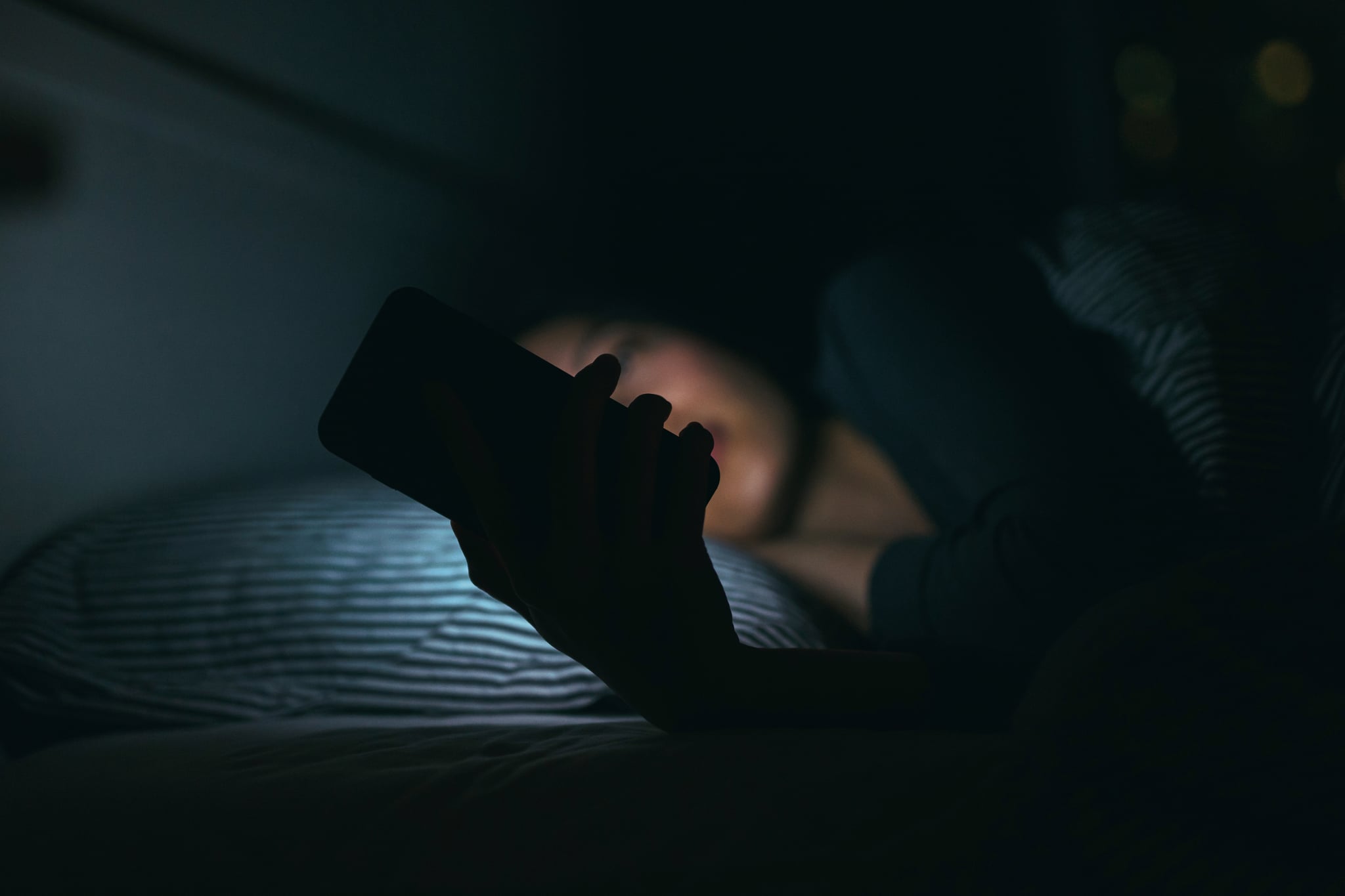 Young woman text messageing on smartphone while relaxing and lying on bed at night