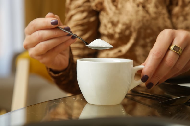 Woman adding sugar to hot drink.