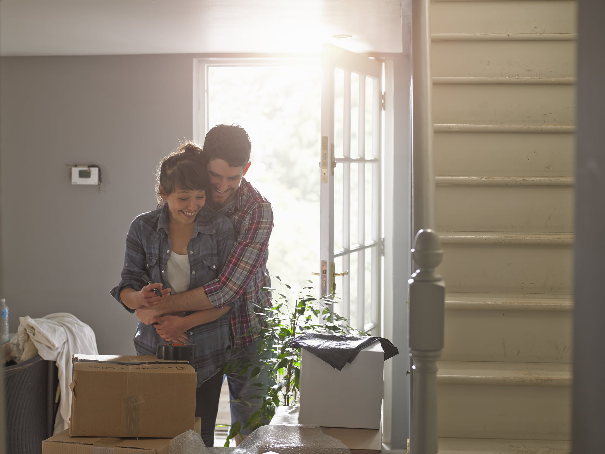 A young professional couple hugging playfully in their home they are surrounded by packing boxes.
