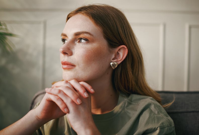 Woman With Red Hair Looking Out Window With Hands Clasped In Front of Her Face