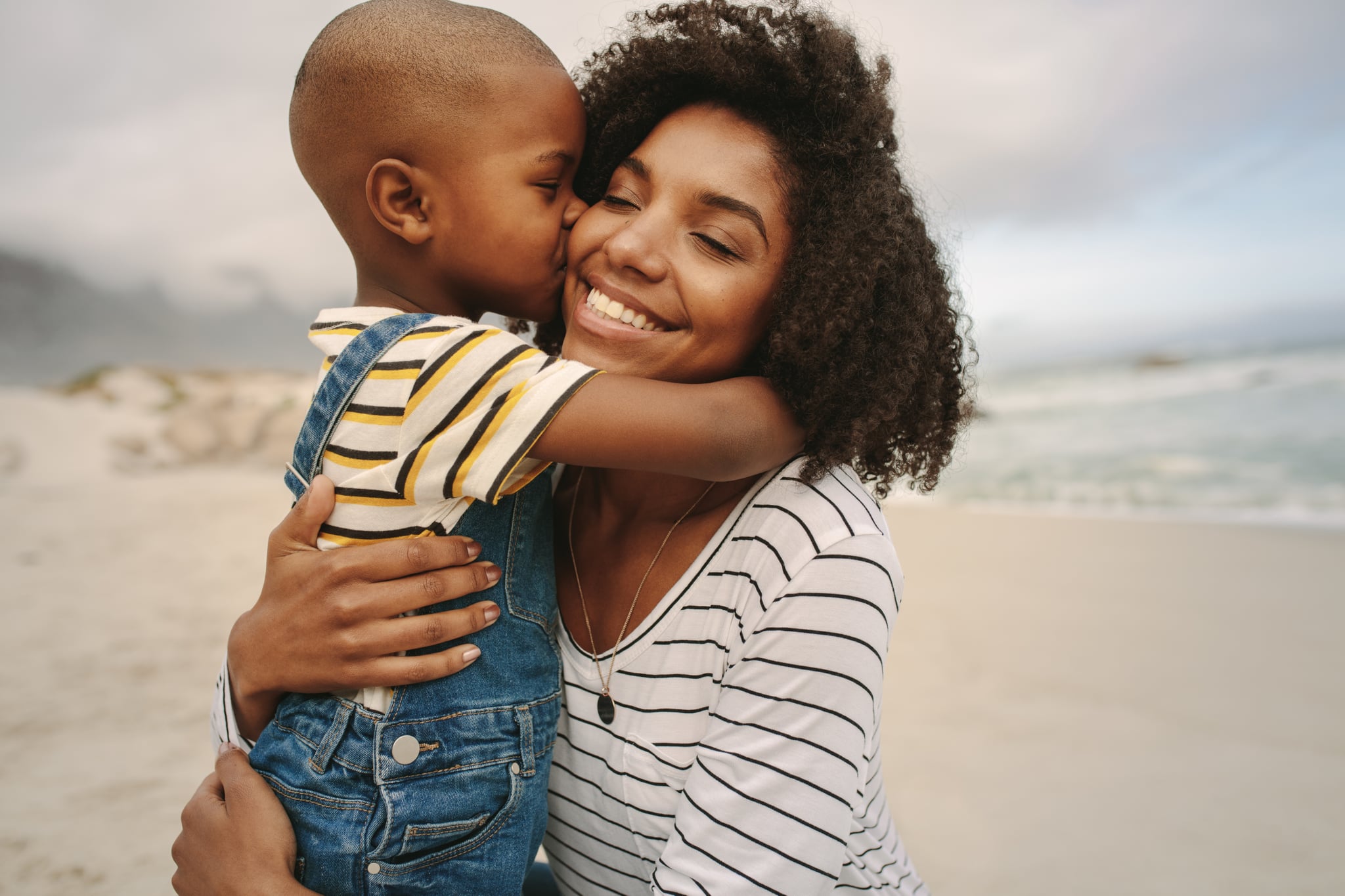 Son kissing his mother at the sea shore. Boy enjoying at day out with his mother on the beach.