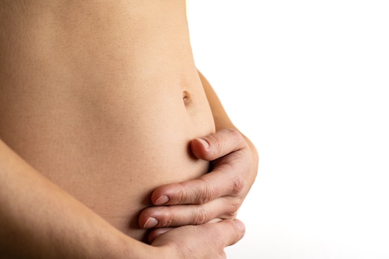 Description: Very close up view of woman in first months of pregnancy gently holding her belly. Pregnancy first trimester - week 18. Close up. Side view. White background. Bright shot.