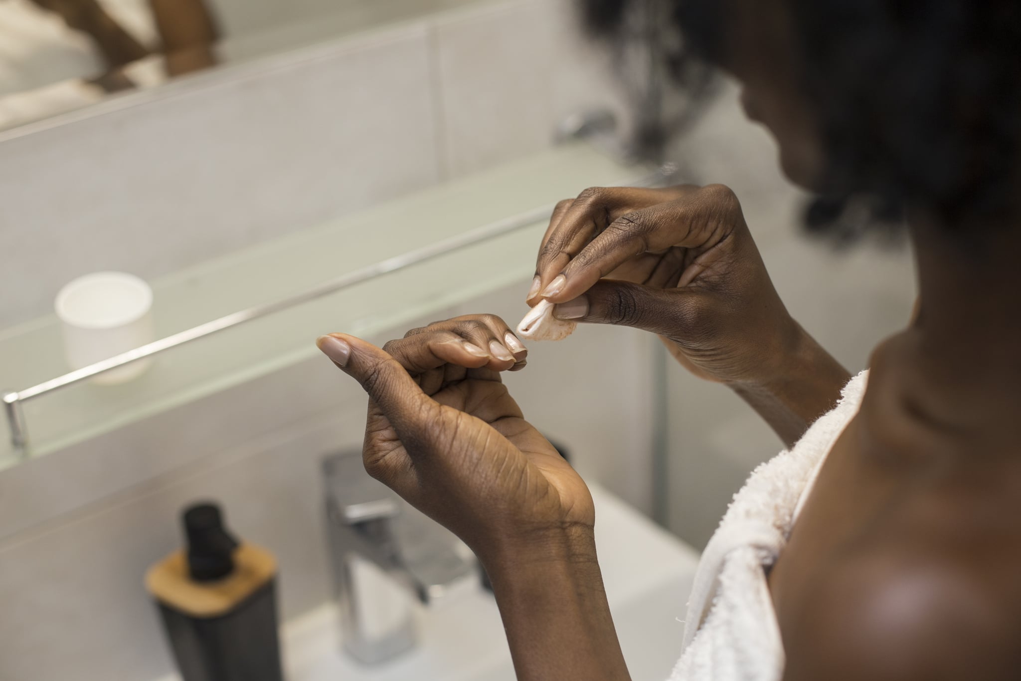 Unrecognisable African female removing her nail polish.