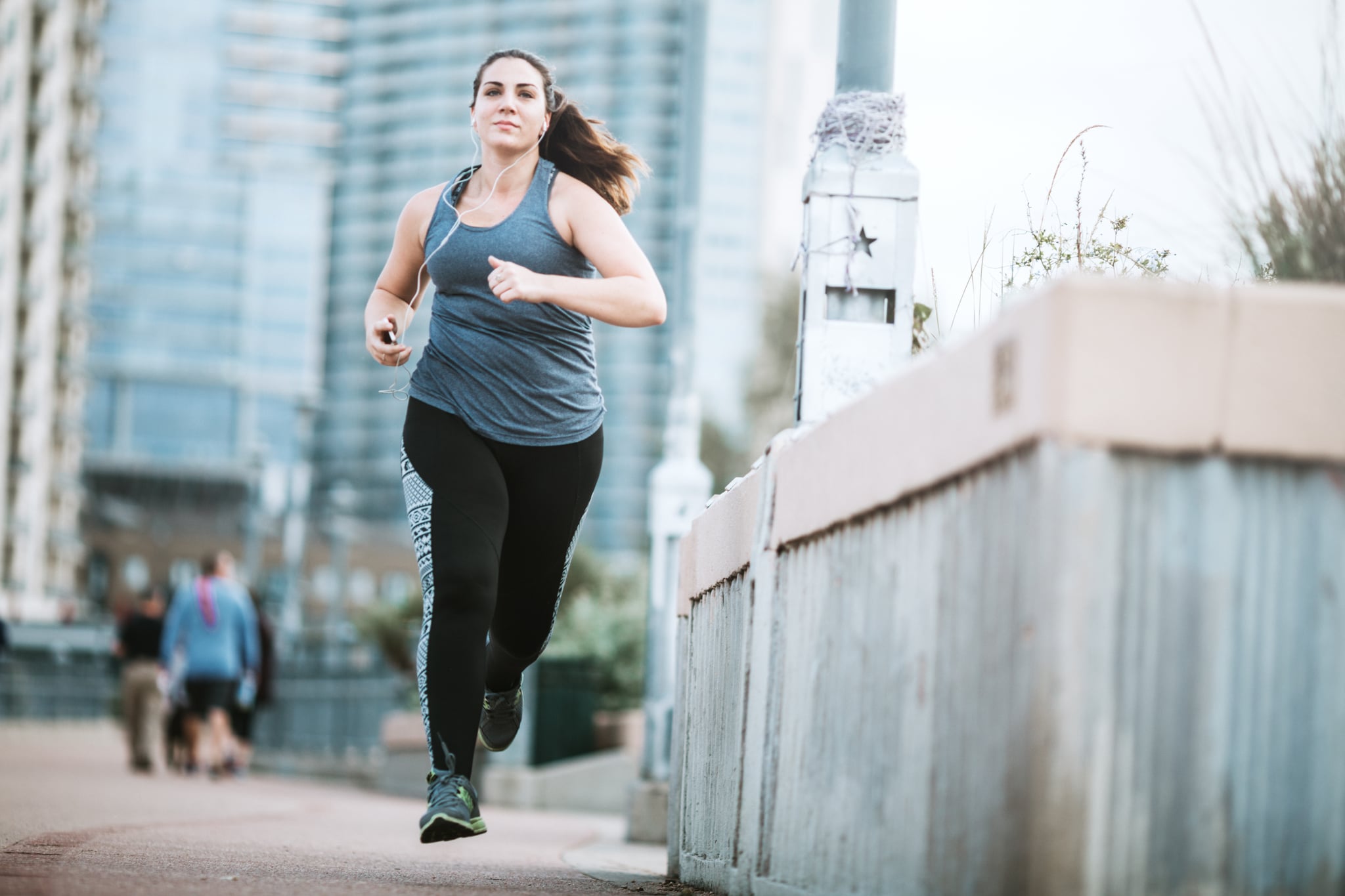 A young adult woman goes for a morning run, crossing the Lamar Street pedestrian bridge in Austin, Texas.  The bridge gets a large volume of foot traffic in the morning with people exercising at the start of their day.  She has a focussed look of determination, listening to music on her smartphone.