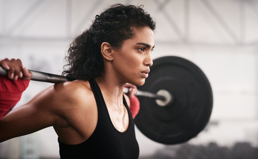 Shot of a sporty young woman lifting a barbell in a gym