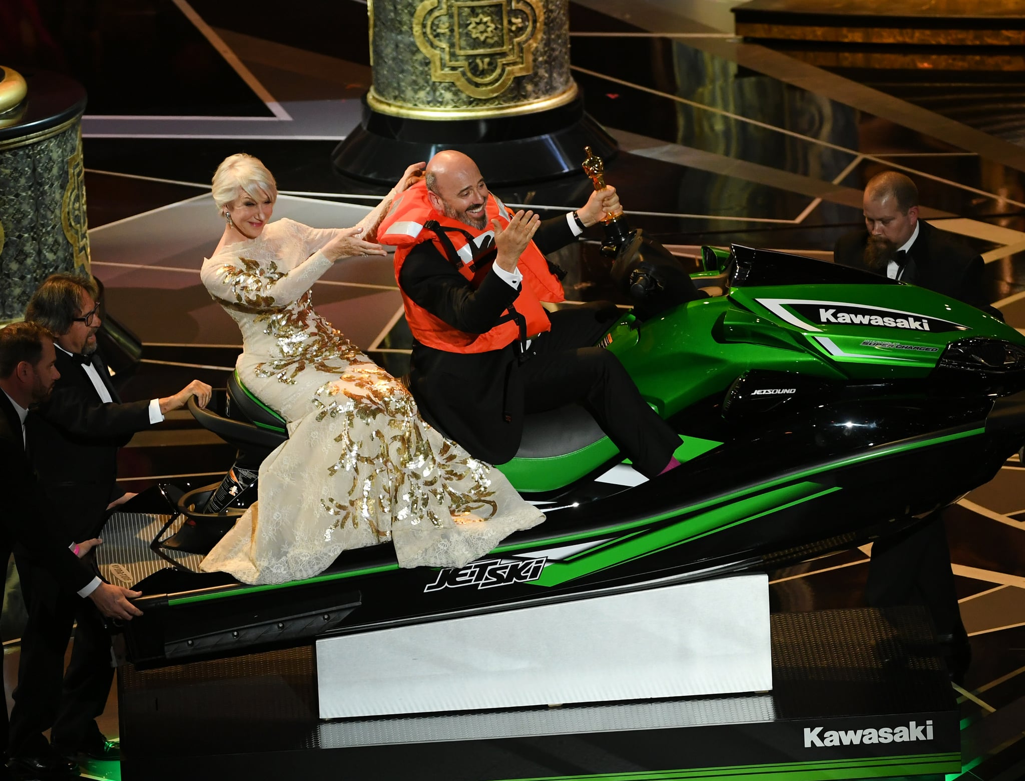 HOLLYWOOD, CA - MARCH 04:  (L-R) Actor Helen Mirren with Oscar-winning costume designer Mark Bridges sitting on a Jet Ski (which he received as a prize for shortest acceptance speech) onstage during the 90th Annual Academy Awards at the Dolby Theatre at Hollywood & Highland centre on March 4, 2018 in Hollywood, California.  (Photo by Kevin Winter/Getty Images)