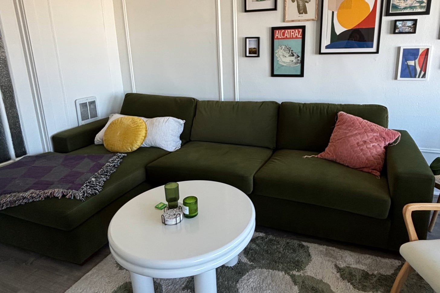 a photo of the albany park barton chaise sectional in a velvet green fabric is pictured, alongside a coffee table and gallery wall in an apartment.
