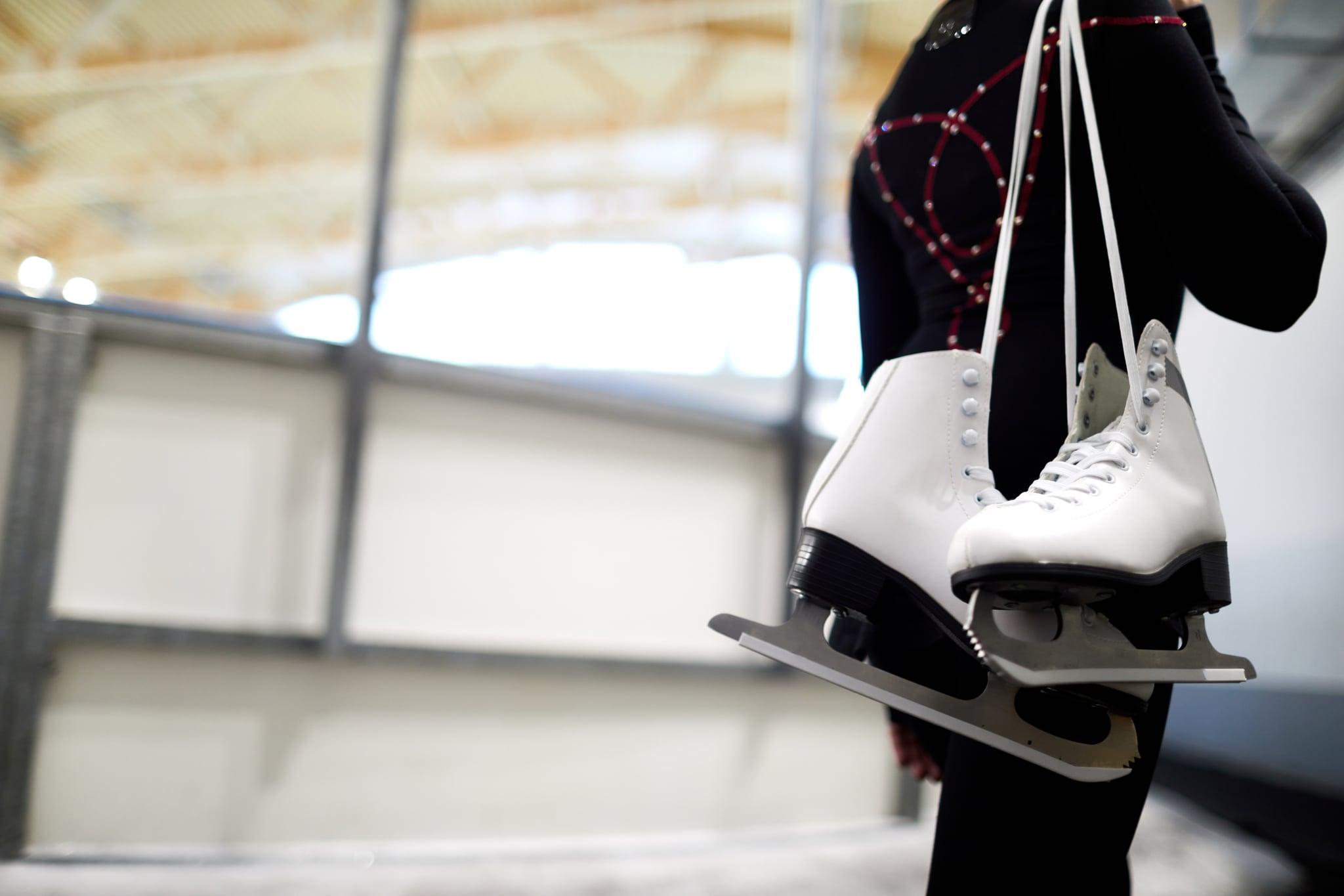 Closeup of unrecognisable girl holding figure skates over shoulder leaving ice rink after sports training, copy space