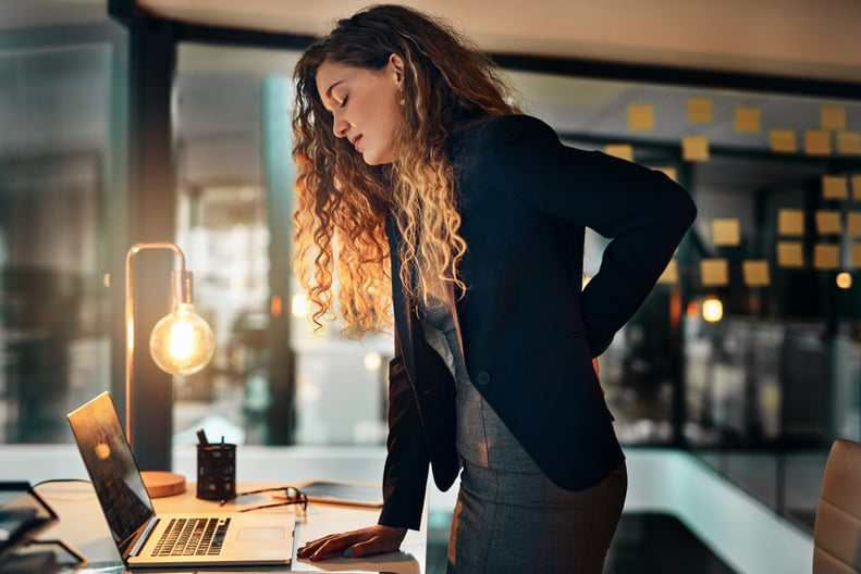 Shot of a businesswoman suffering from back pain while sitting at her desk