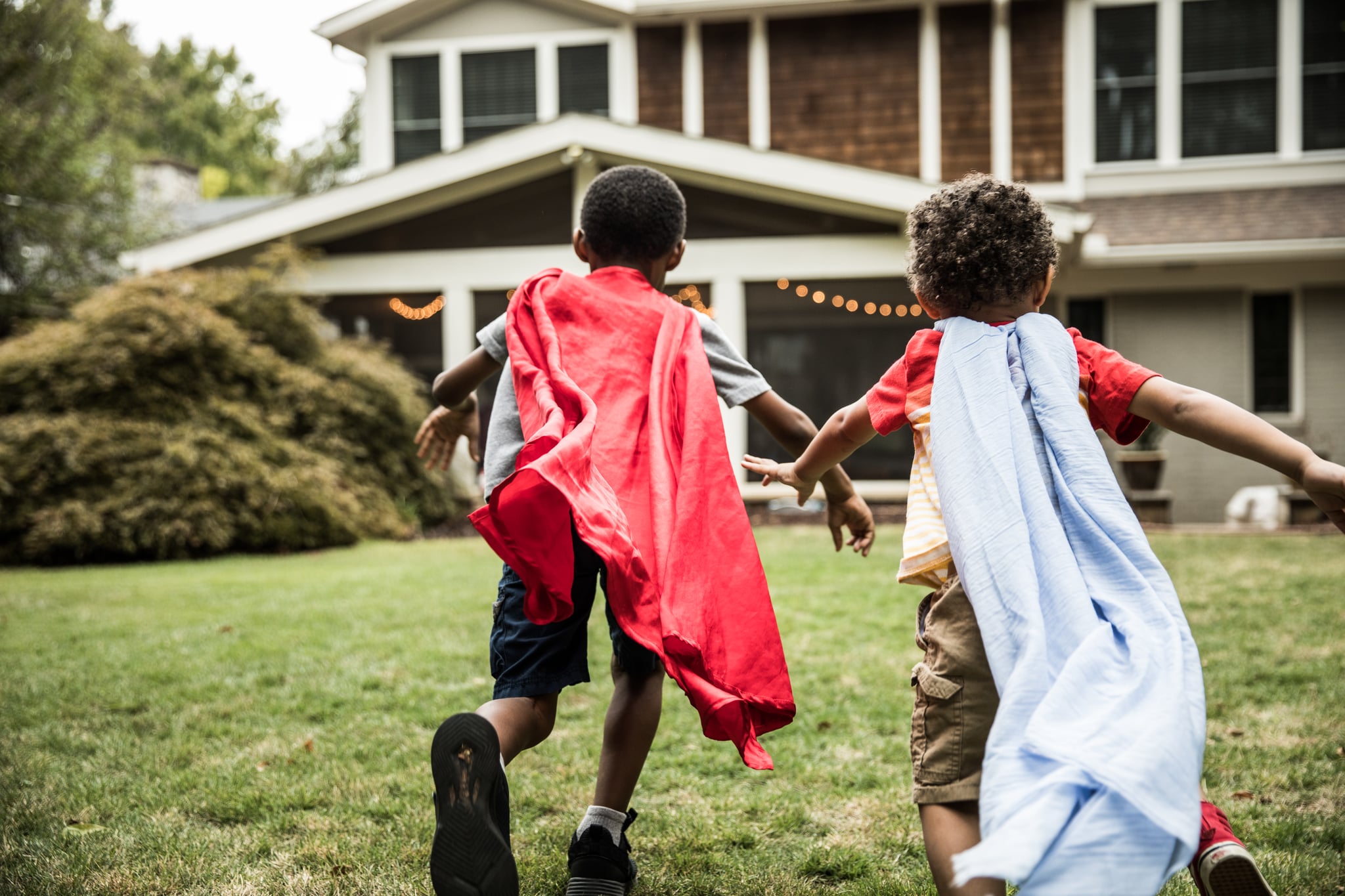 Young boys (3 yrs and 6yrs) in capes playing in backyard