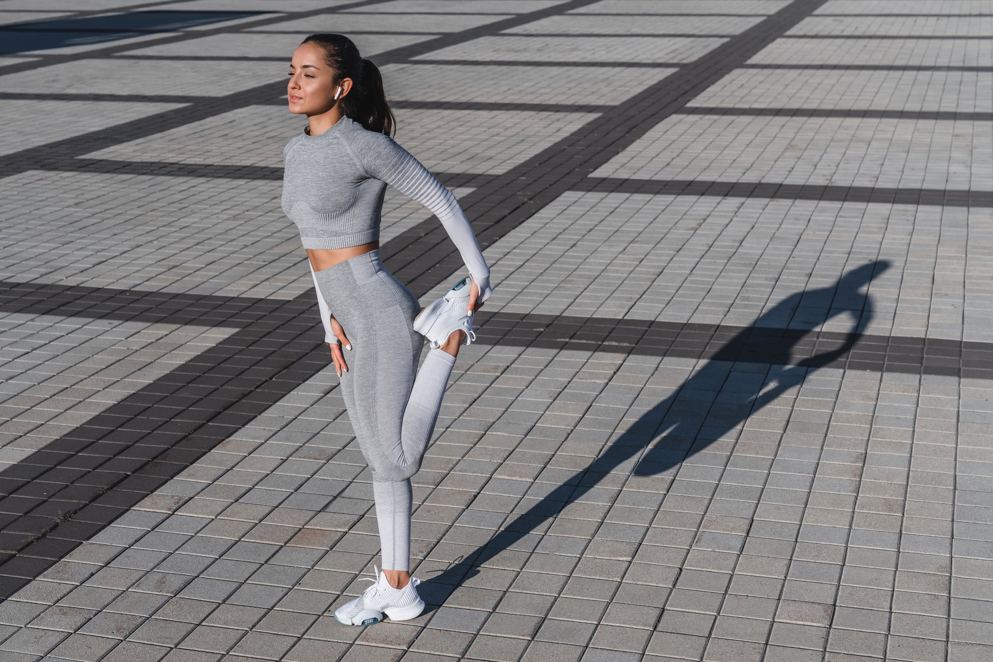 20s beautiful slim girl is exercising her leg after jogging in urban area.