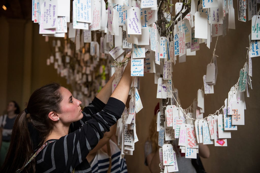 一个女人将她的手写信息挂在树上的笔记在波士顿公共图书馆的纪念展览。